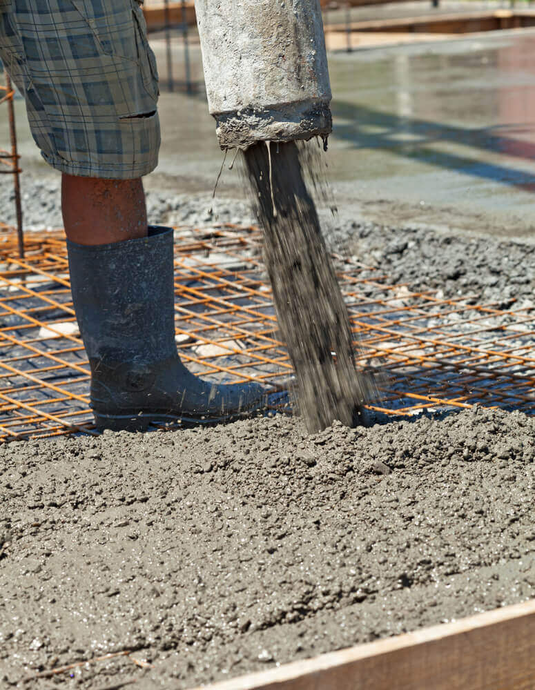 A close up shot of a concreting Ballarat worker pouring wet concrete mix into the steel reinforcement whilst he is wearing concreting boots