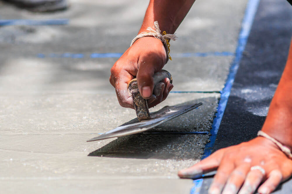 a concrete repair worker fixing the edge of a concrete footpath with a concrete tool