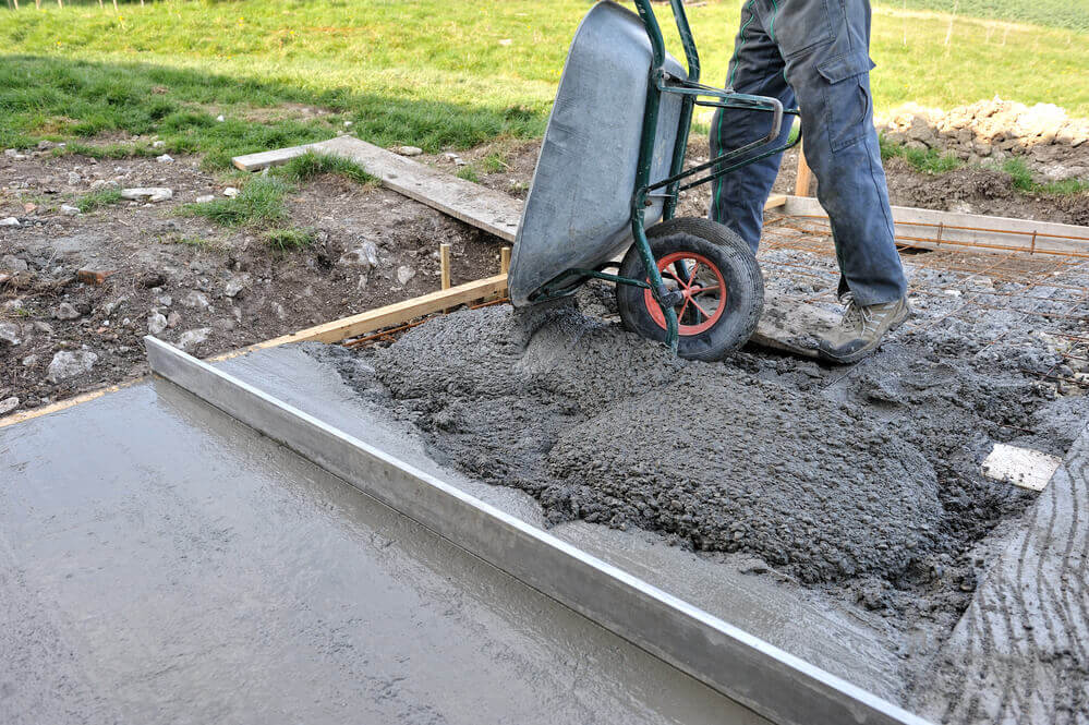 a worker pouring a wheelbarrow full of concrete into some concrete slabs that is being made with wood surroundings 