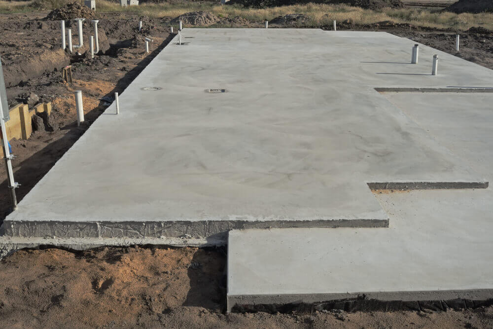 One of our new concrete slabs with the pipes coming up from the ground and dirt around the outside of the slab